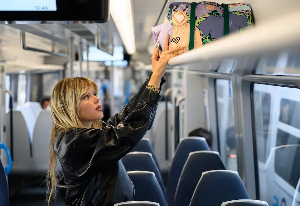 Model placing the Trainline Re-Fresher Bag on an overhead train rack