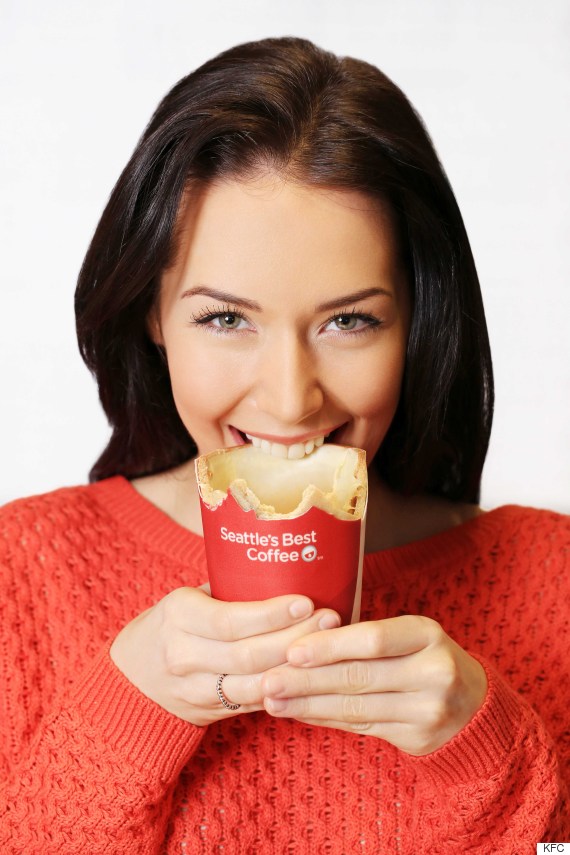 Woman biting into the KFC Scoff-ee Cup, showing the edible biscuit cup wrapped in Seattle's Best Coffee branded sugar paper