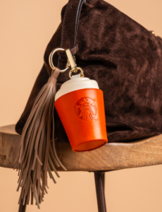 Starbucks The Autumn Charm leather coffee cup bag charm with tassel clipped to a brown handbag by The Robin Collective