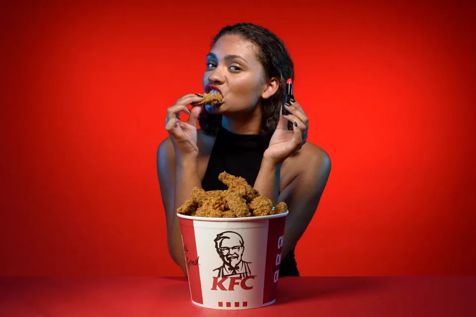 Model wearing KFC chicken-flavoured lipstick eating from a KFC bucket - The Robin Collective